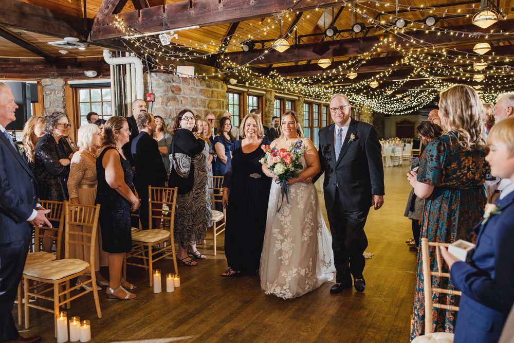 Wedding reception venue decorated with string lights and wooden chairs as guests celebrate on dance floor.