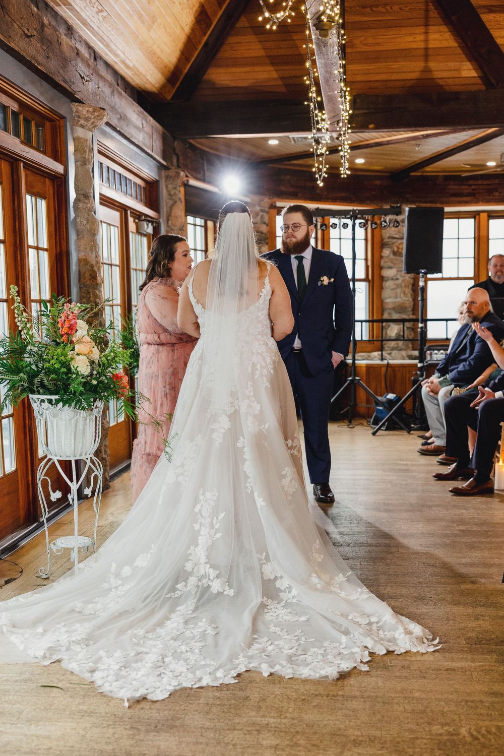 Wedding dress train with intricate lace details sweeps across rustic wooden floor in elegant venue.