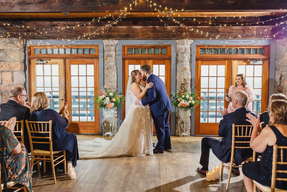 Rustic wedding venue with string lights hanging from wooden beams and large windows letting in natural light.