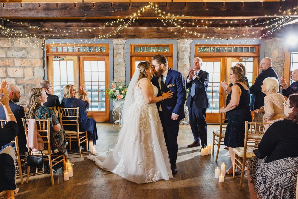 Panoramic view of wedding ceremony in rustic stone venue with string lights and wooden accents.