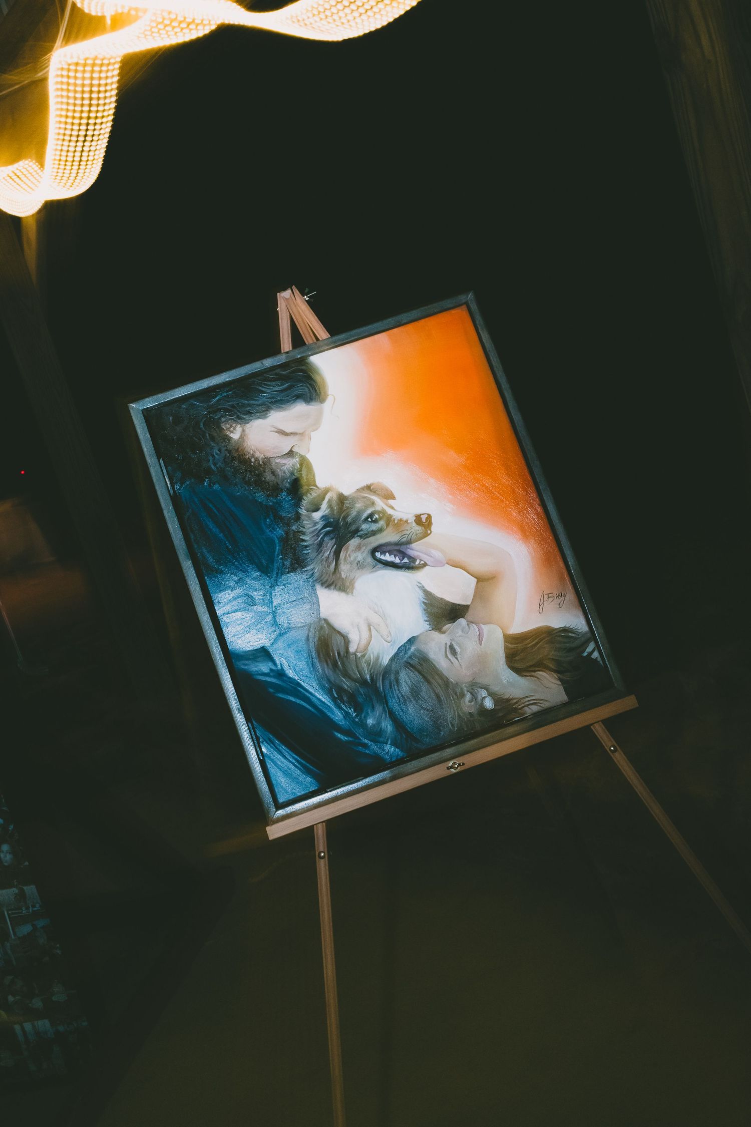 Illuminated art display on an easel showing a portrait in moody lighting with dramatic orange glow from above.