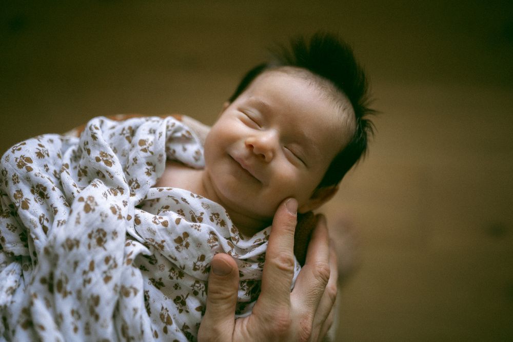 A baby in a white floral onesie lies on a bed while showing different emotional expressions in a photo series.