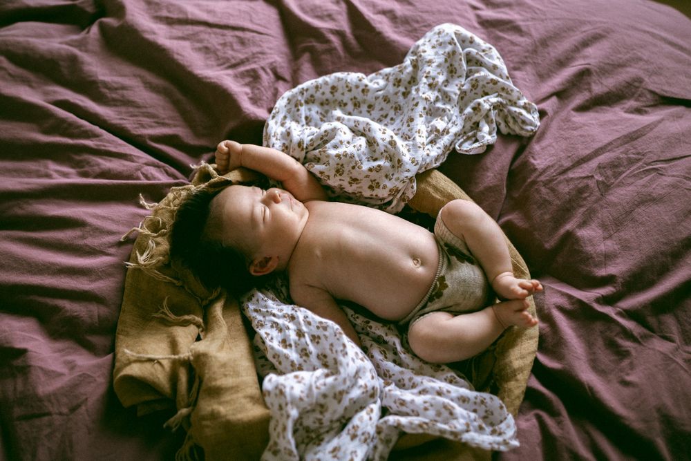A sleeping baby lies on burgundy bedding with white lace fabric draped nearby.