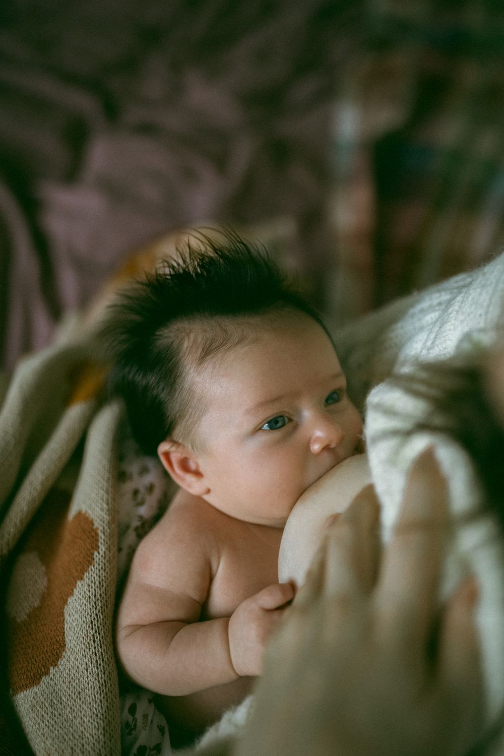 A baby drinks from a bottle while lying down on a soft cushion surface.