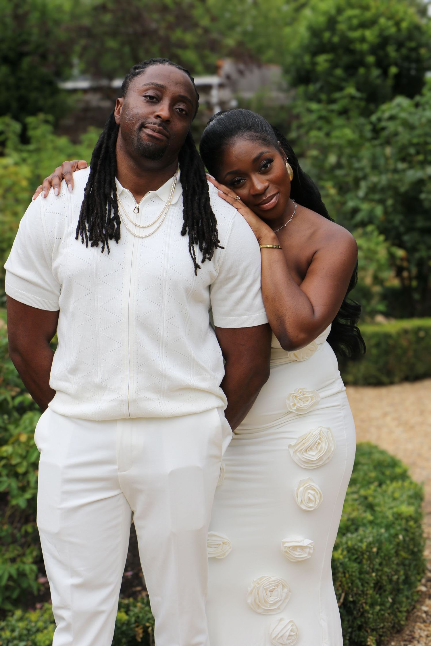A couple embraces in a romantic outdoor setting with tall grass and green trees in the background.