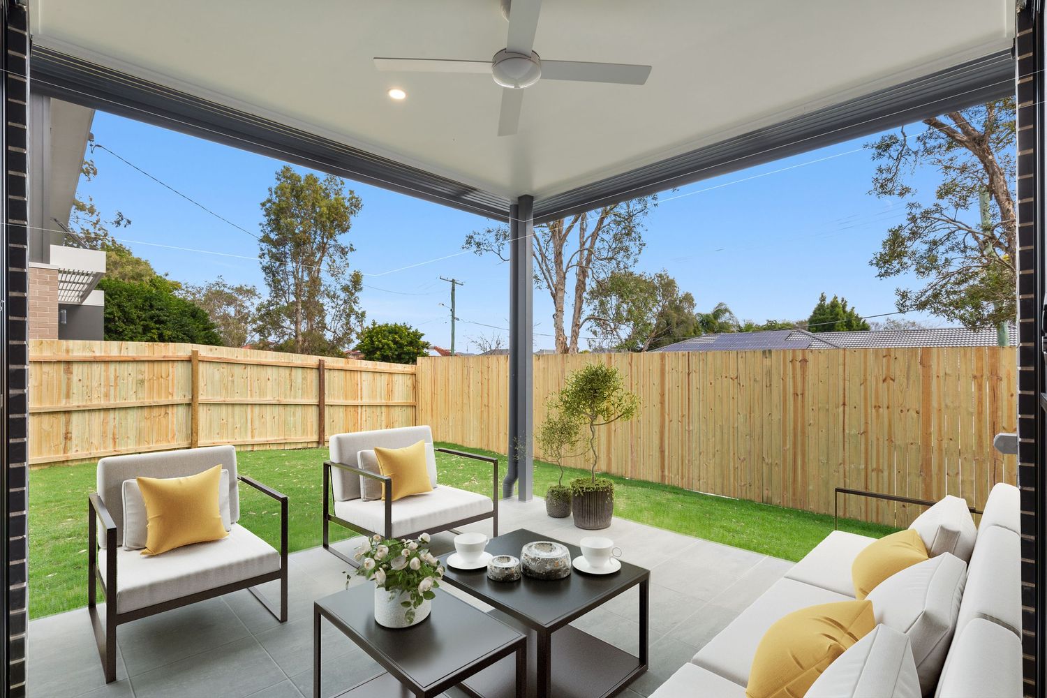 Modern covered patio with outdoor lounge, ceiling fan, and timber fence backdrop.