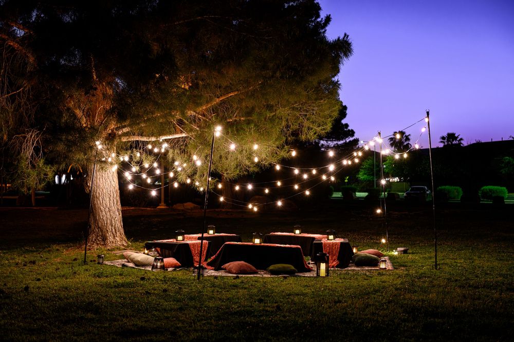 String lights illuminate a romantic outdoor dining setup with tables and chairs under trees at night. Branding photography Las Vegas