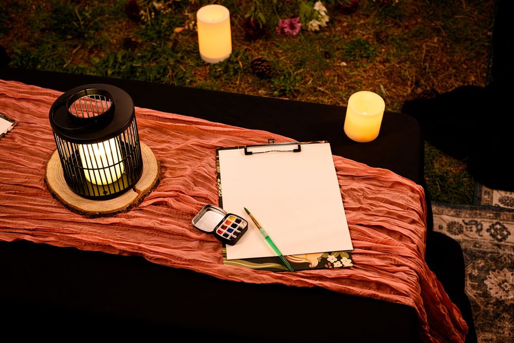 A table with blank papers, lantern light, and candles creating a cozy evening writing setup outdoors. Branding photography Las Vegas