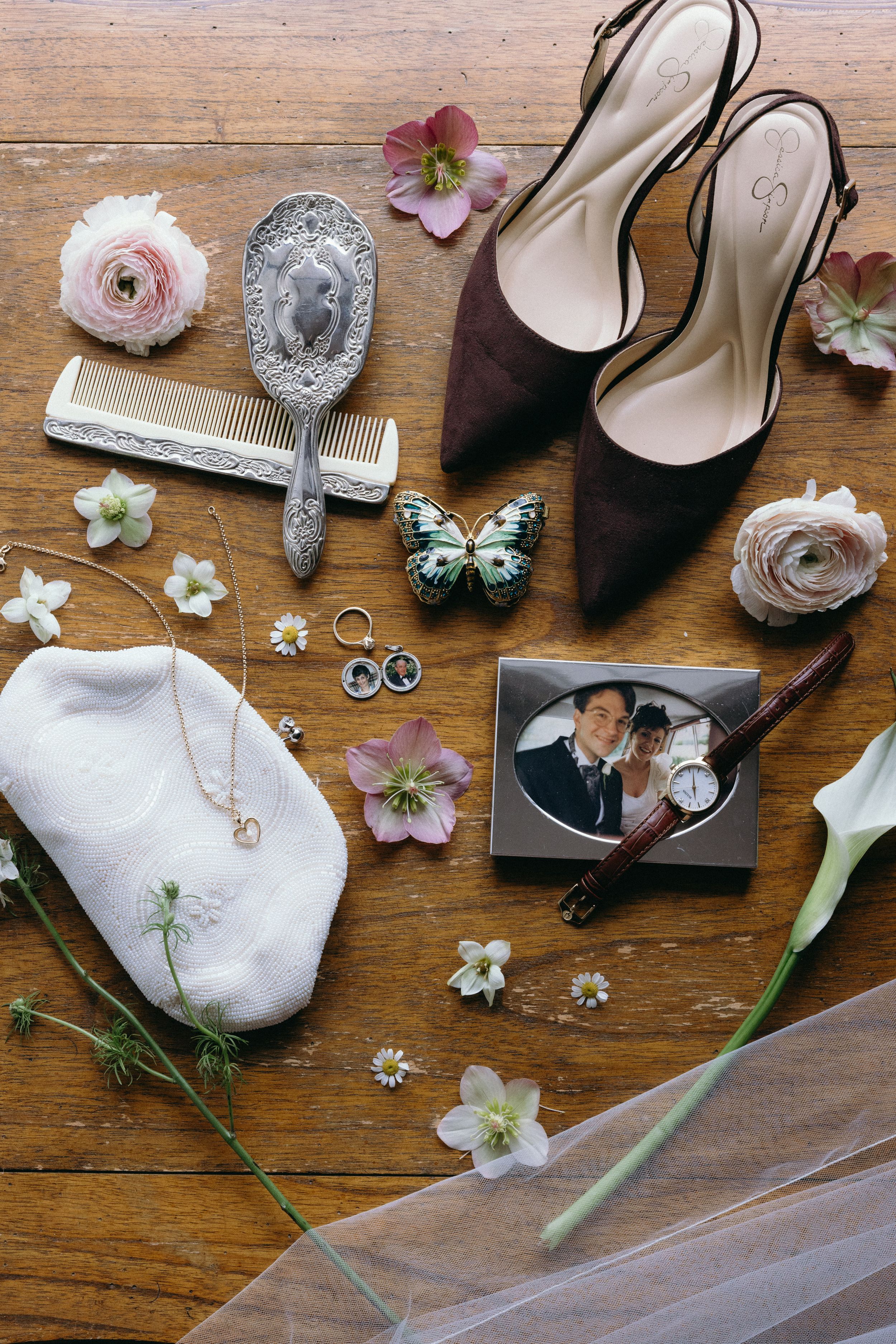 Wedding accessories including vintage shoes, flowers, jewelry, and decorative items arranged on wooden surface.