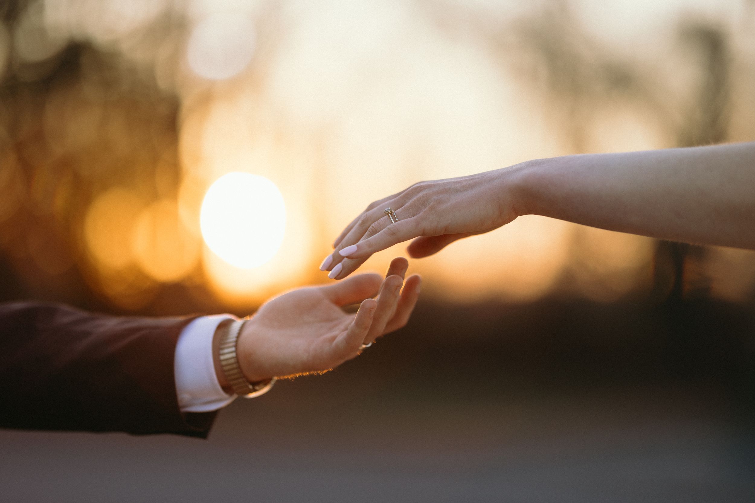 Two hands reach towards each other against a warm sunset background creating a silhouette effect.