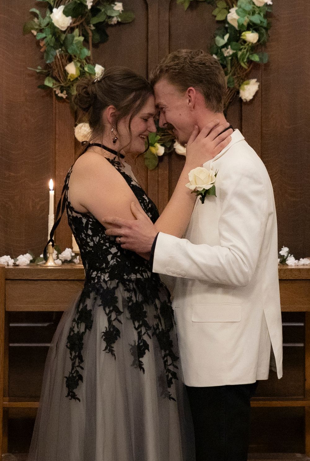 A couple in formal attire share a romantic dance moment under floral decorations at an indoor venue.