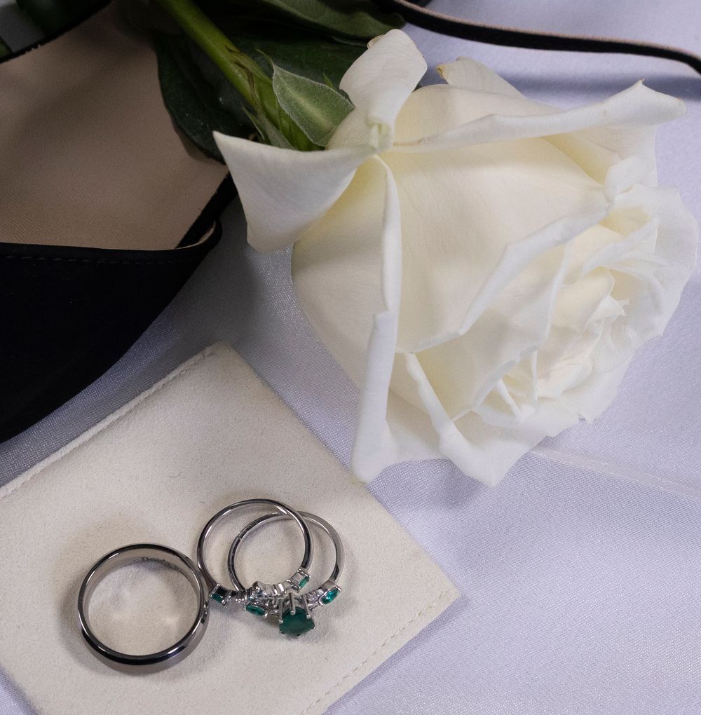 White rose petals and silver rings with blue gemstones arranged in an elegant wedding detail shot.