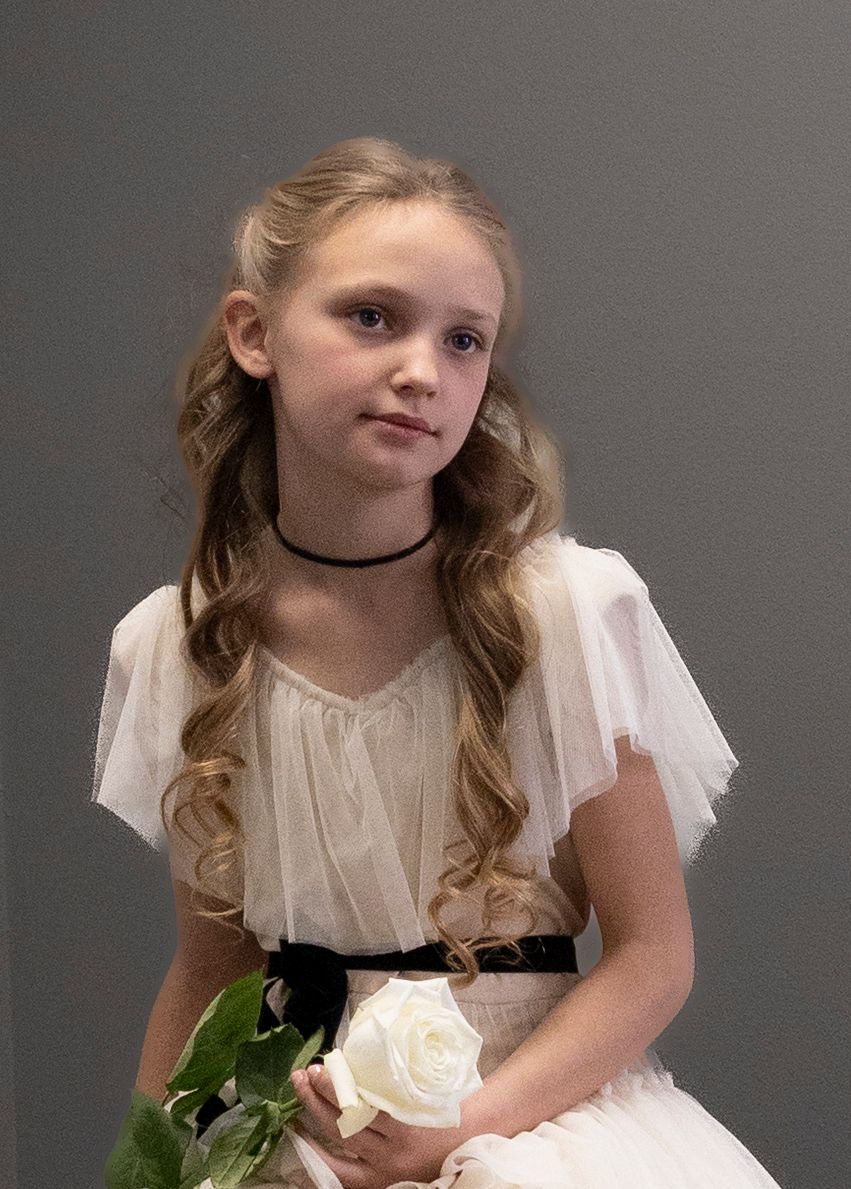 Young girl in white dress with fluttering sleeves holding a white rose against a gray background.