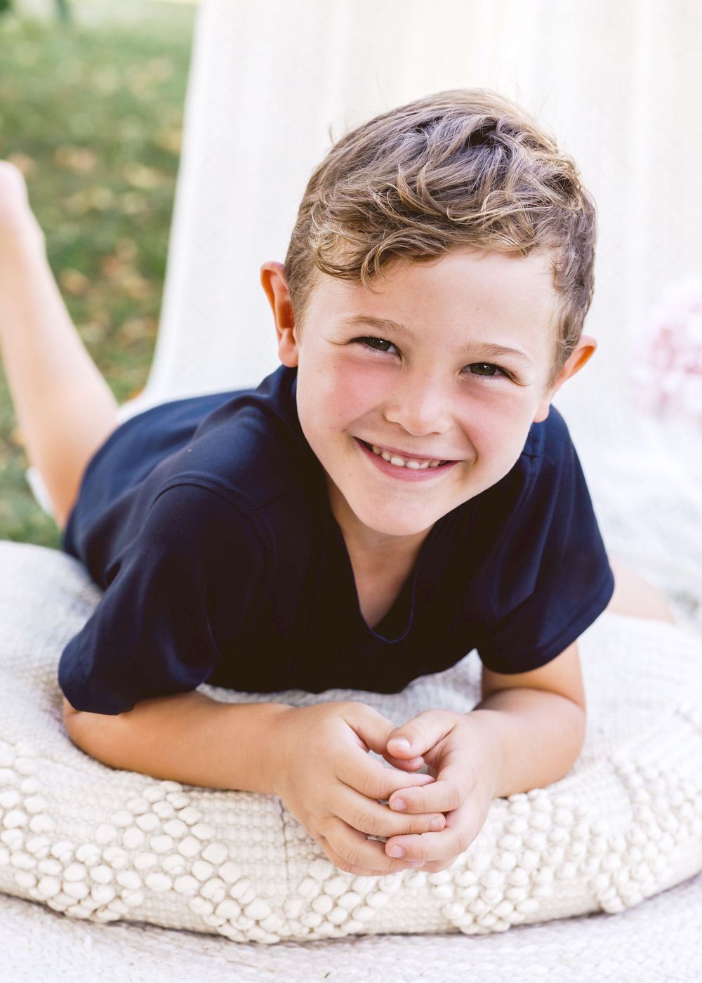 Child in navy blue t-shirt lying on textured white blanket with joyful expression.