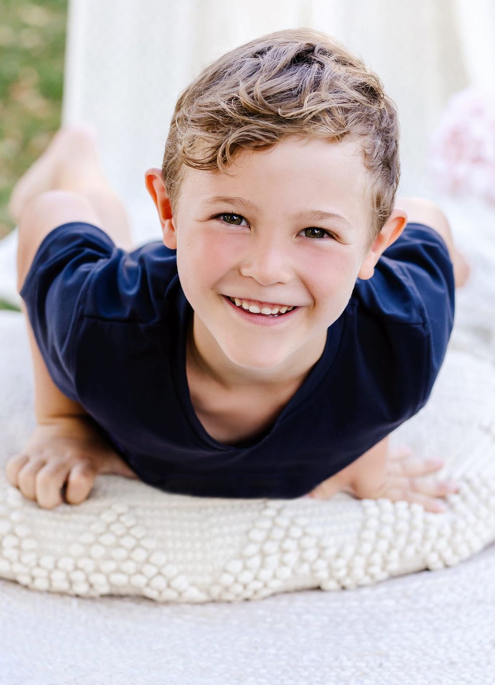 Young child lying on a knitted cream-colored pillow wearing a navy blue sweater.