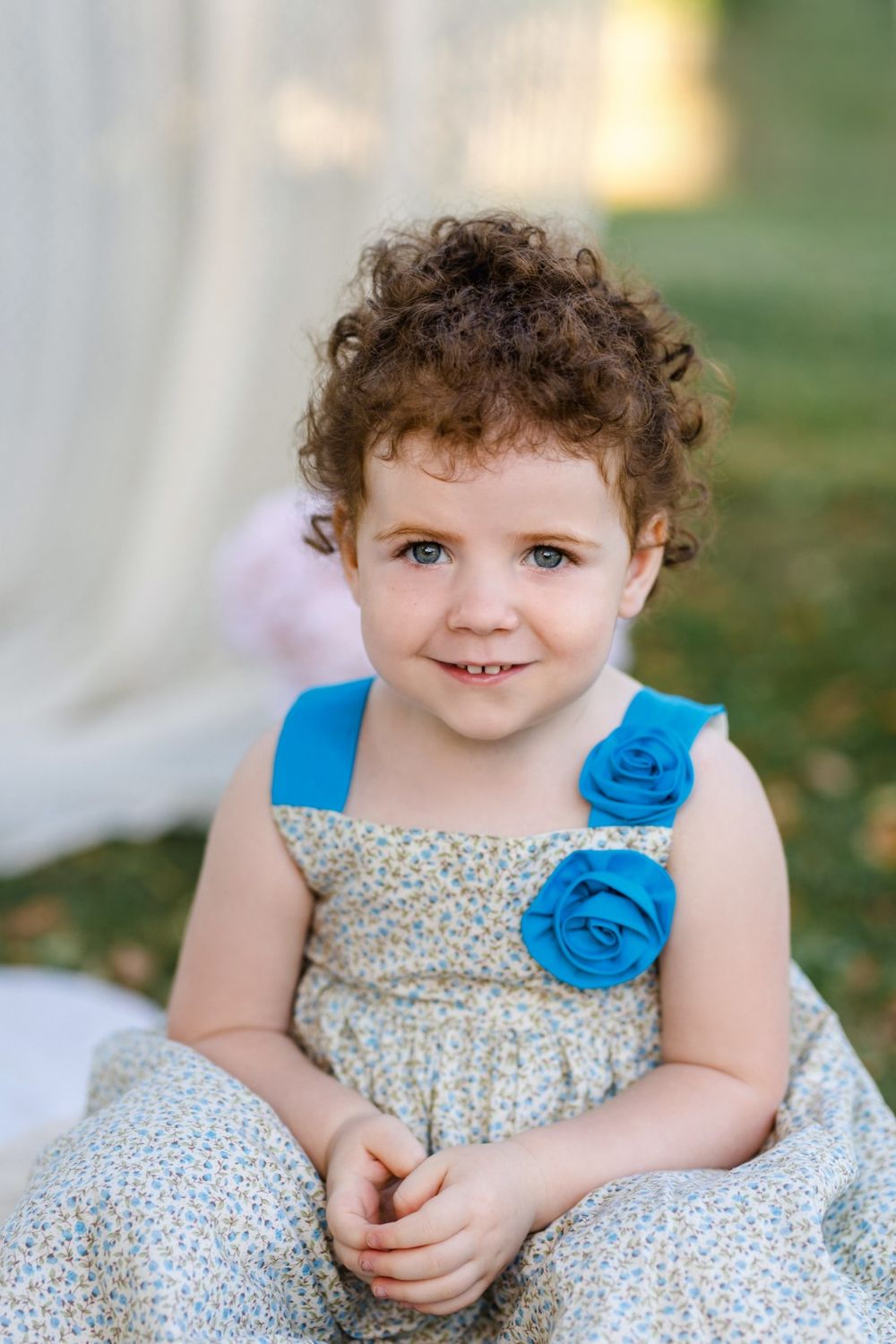 Child wearing floral dress with blue flower accent sitting outdoors in natural lighting.