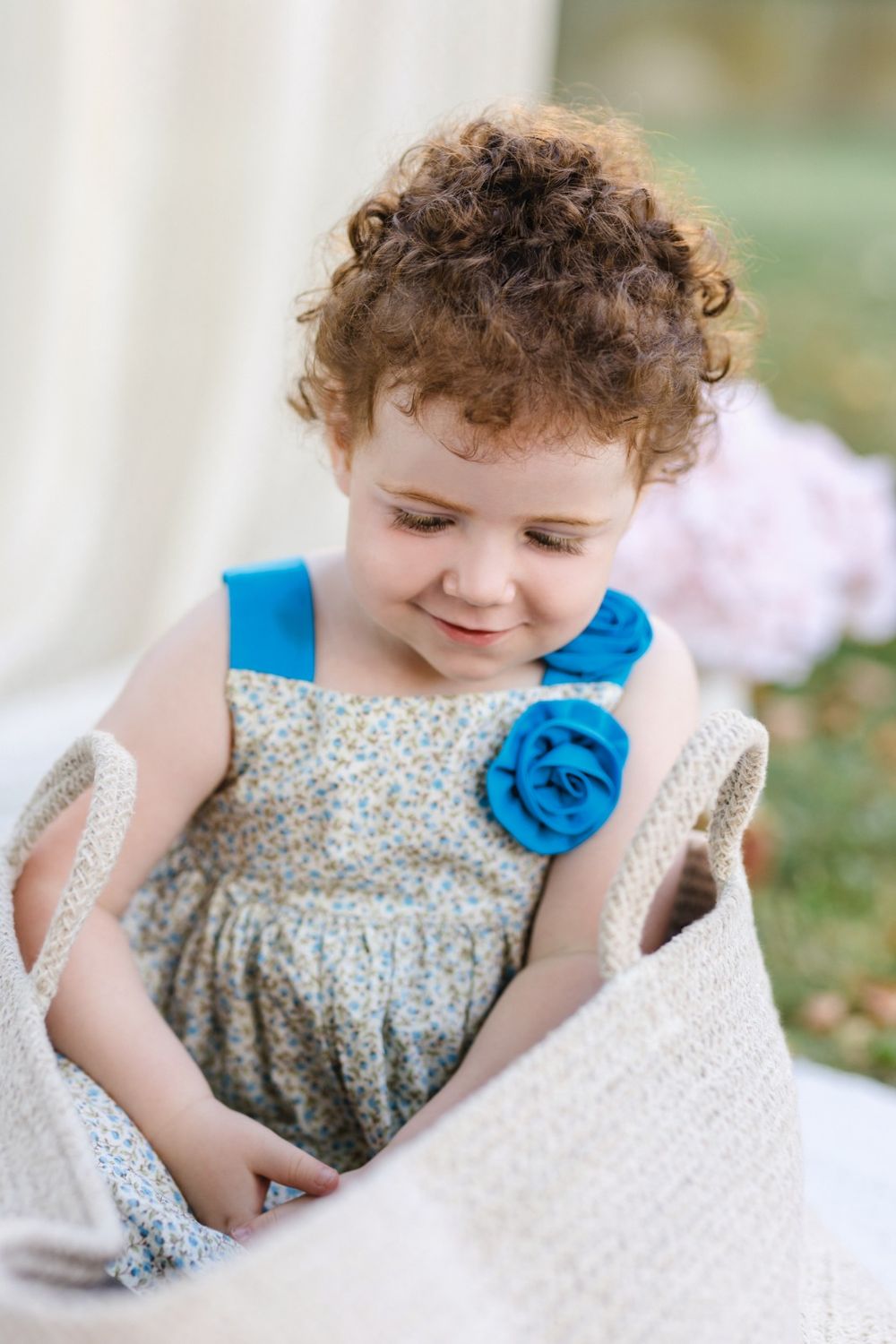 A child in a floral dress plays with white fabric while sitting outdoors on a sunny day.