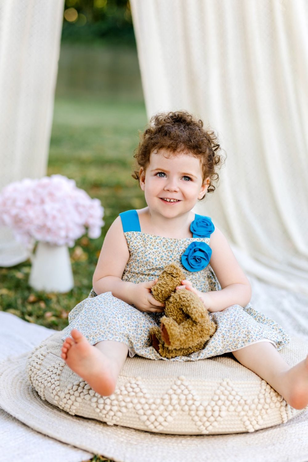 A series of four photos showing a baby sitting on a textured pillow with a teddy bear in an outdoor garden setting.