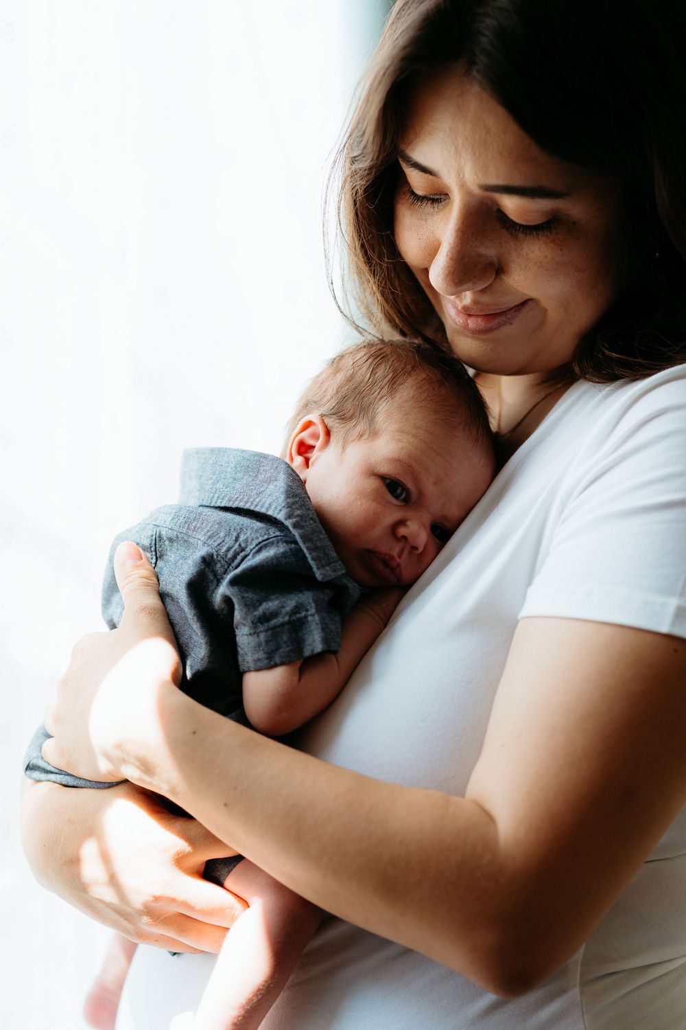 Tender moment between parent and newborn baby in soft natural light against white background.