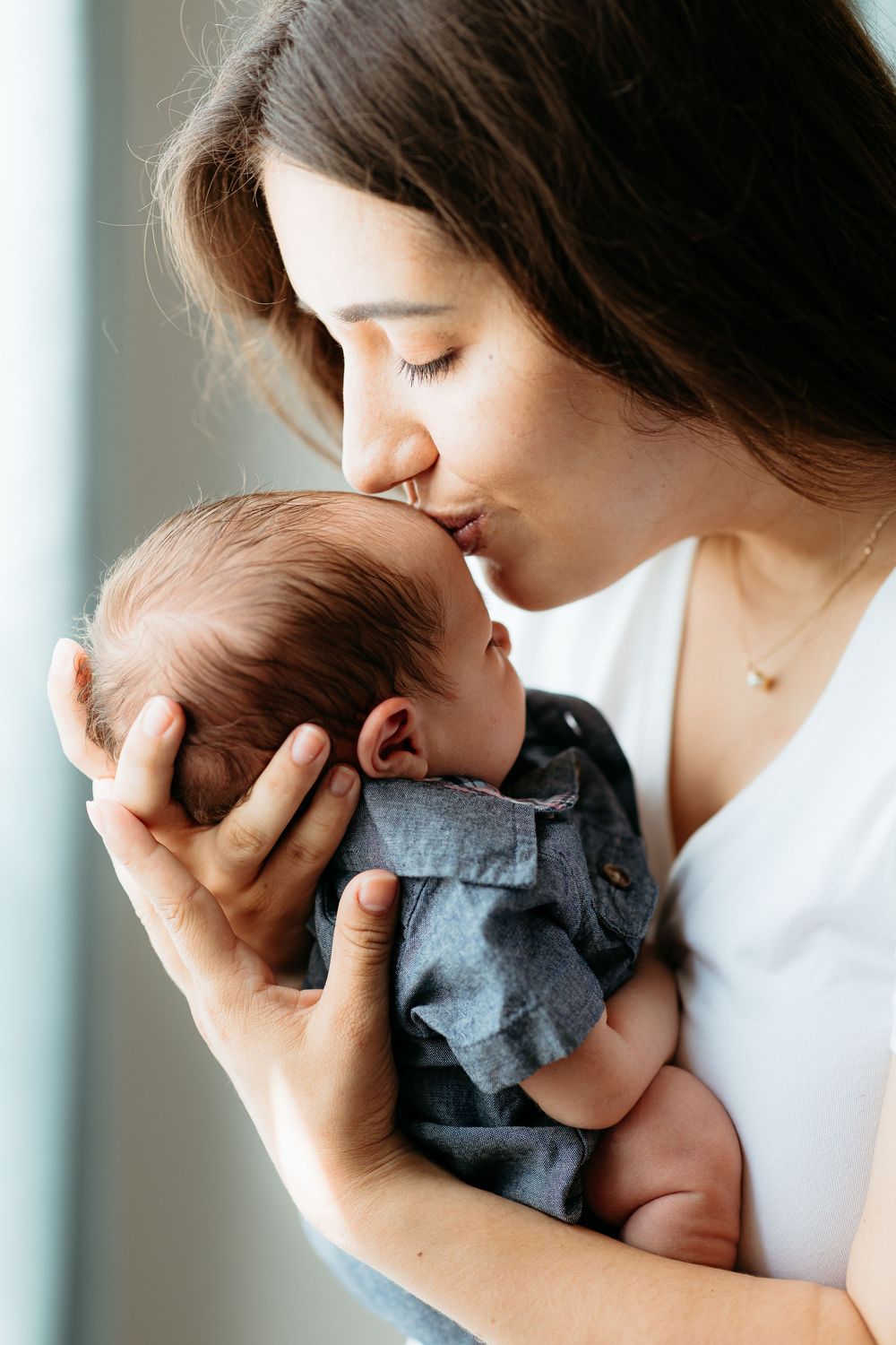 Intimate bonding moment with newborn wearing grey outfit against light background with mother. In-home newborn photos in Central Michigan