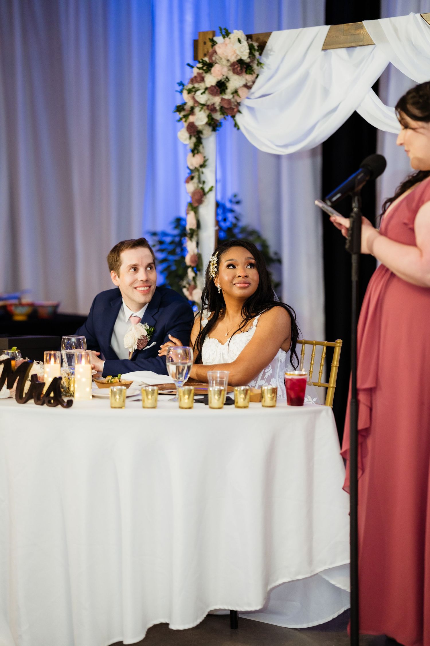 Wedding party members in mauve dresses seated at a long head table during reception dinner.