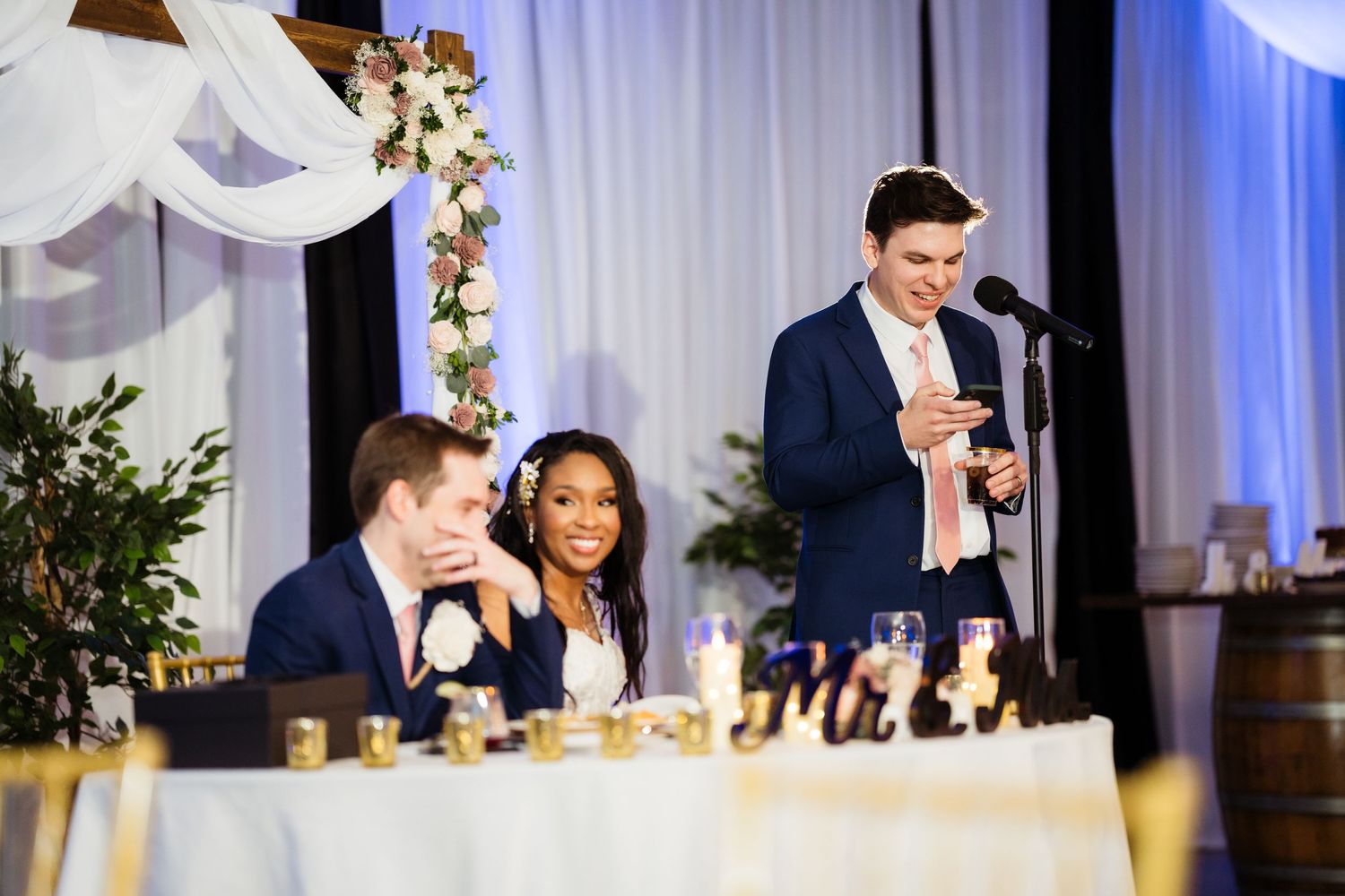 Wedding reception guests seated at elegant tables with white linens and floral centerpieces during evening celebration.