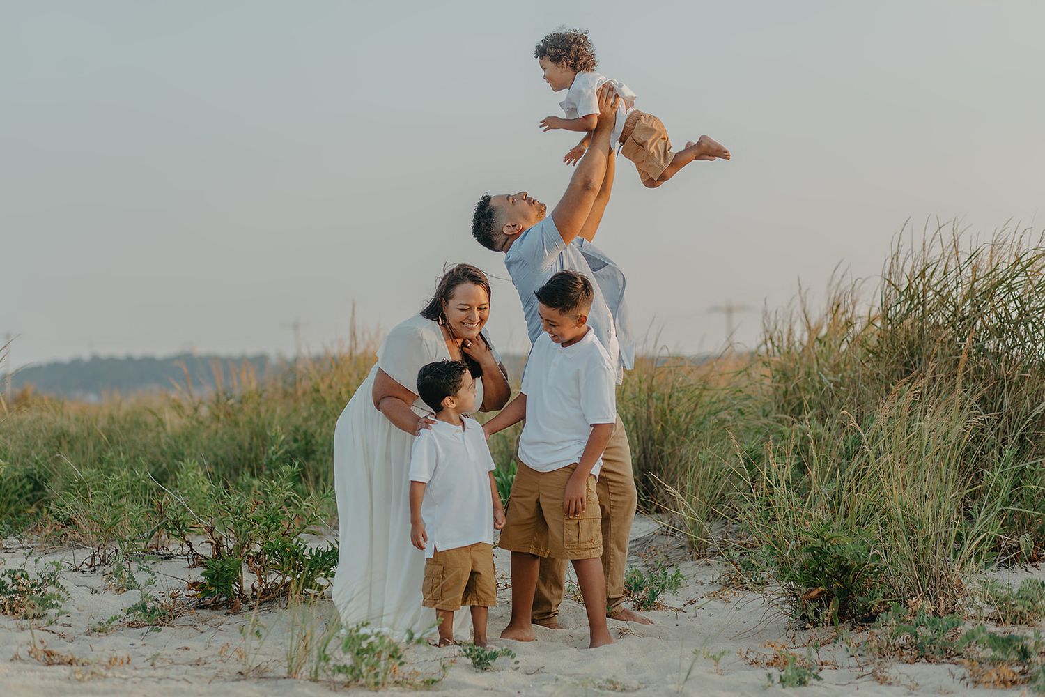 A family sits together and laughs joyfully on a sandy beach during golden hour.