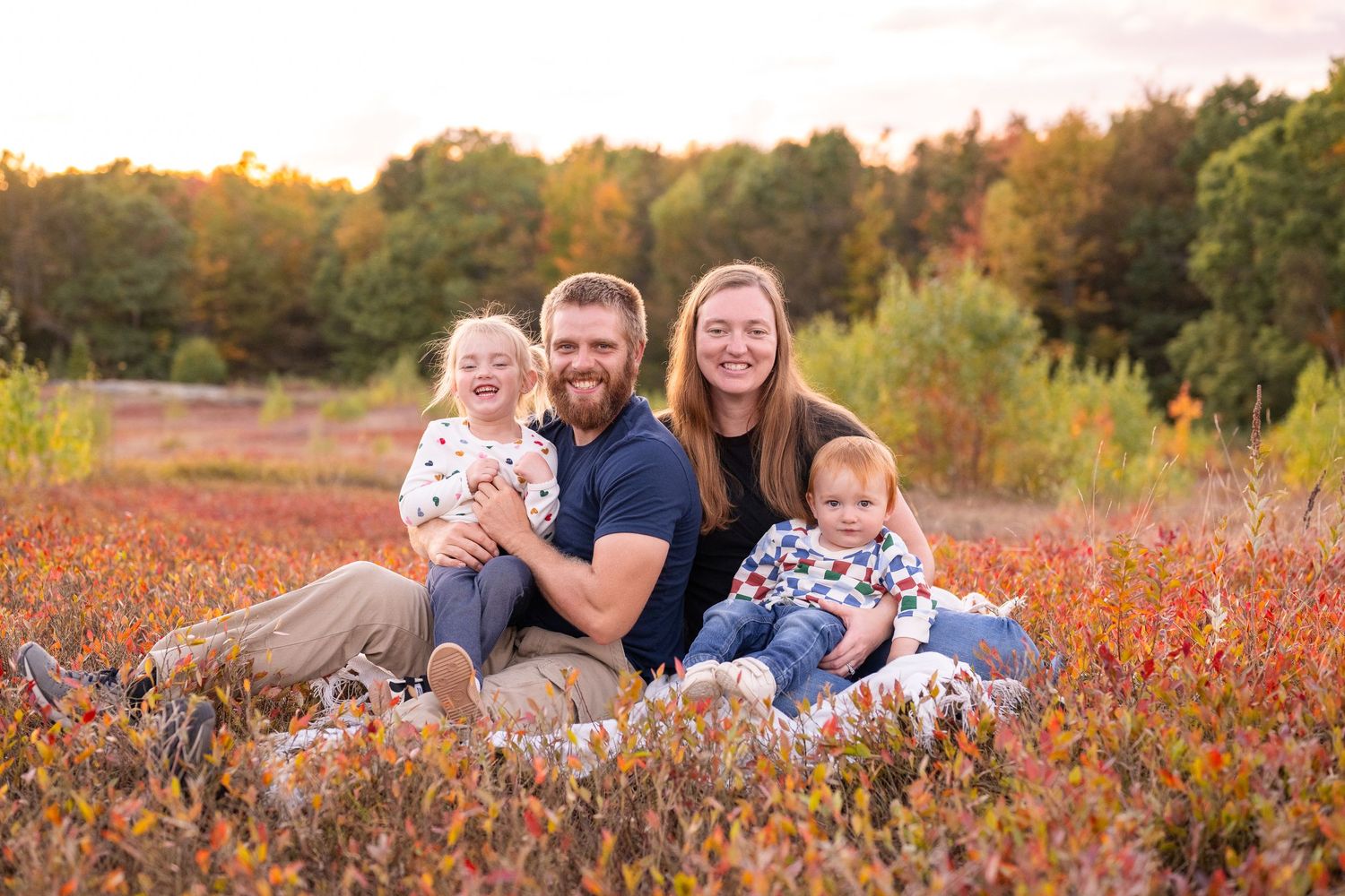 A family walks through a golden autumn field at sunset while holding hands and enjoying the warm evening light.