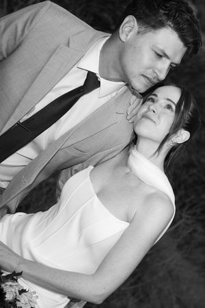 Black and white romantic portrait of bride and groom embracing, groom in grey suit with dark tie.
