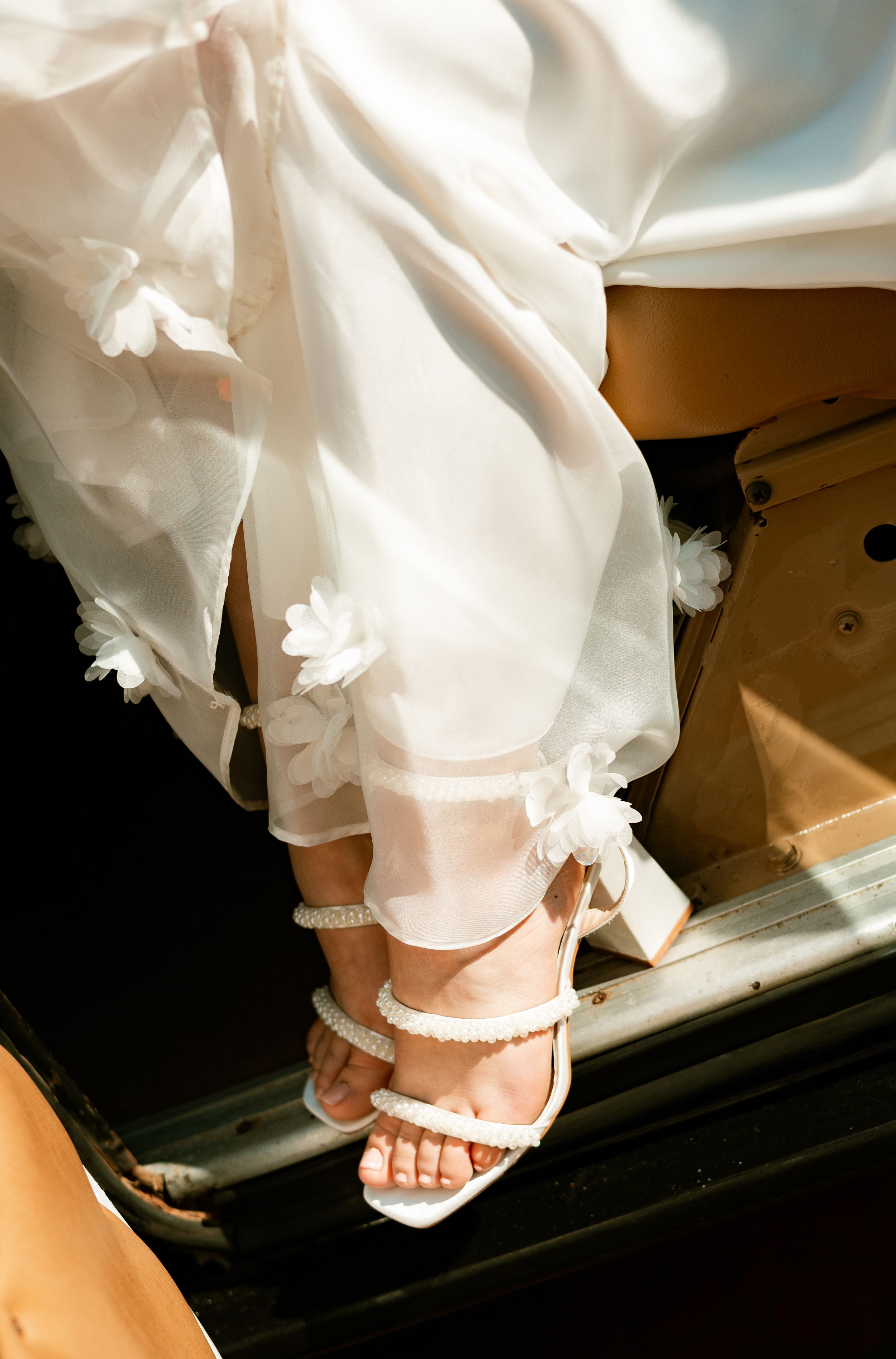 Bride stepping out in white strappy heeled sandals with pearl details and floral organza gown hem.