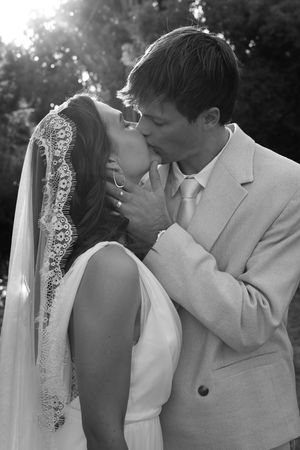 Black and white photo of a bride and groom sharing a kiss outdoors on their wedding day.