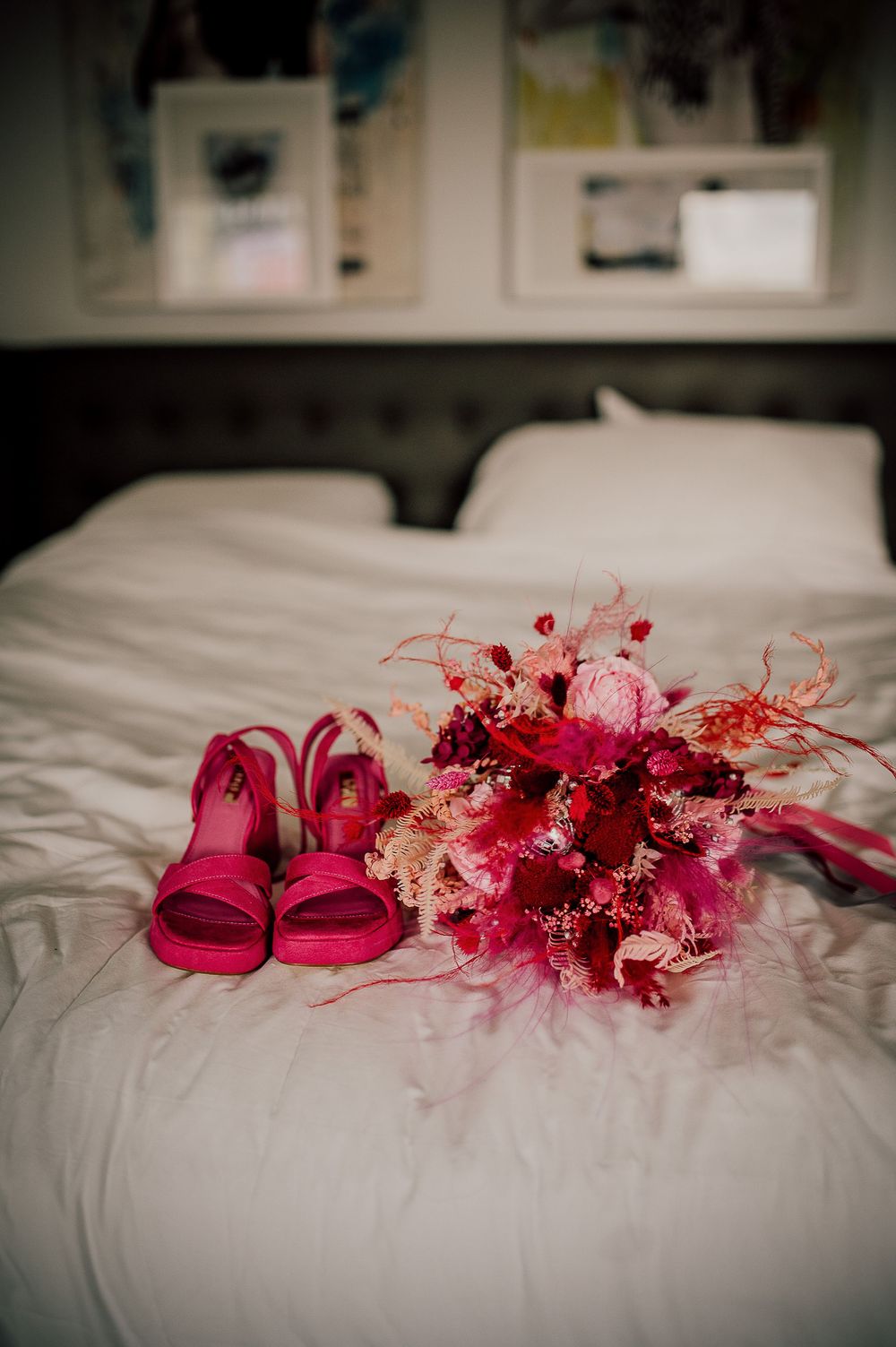 Pink sandals and dried flowers arranged on white bedding create a romantic wedding day detail shot.