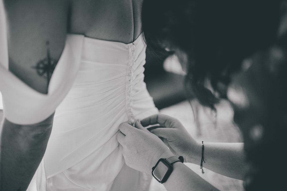 Black and white photo showing someone helping to button or adjust a white wedding dress.