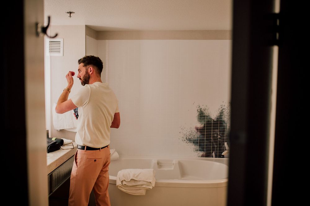 Person in khaki pants and white shirt getting ready in a modern bathroom with white tub and plant decor.