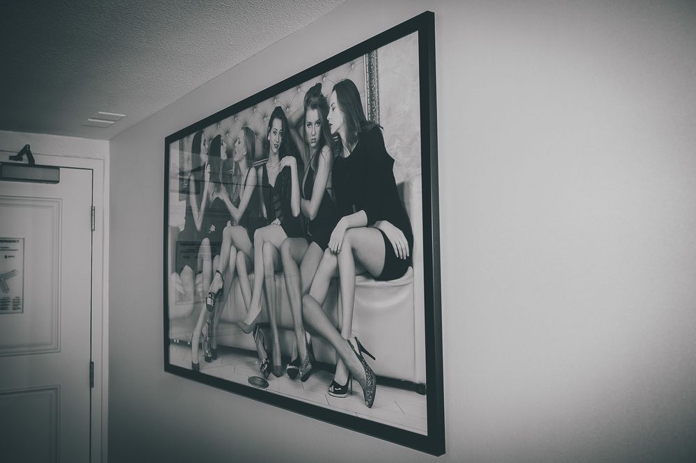 A black and white framed photograph hanging on a white wall shows a vintage group beach scene with a volleyball.