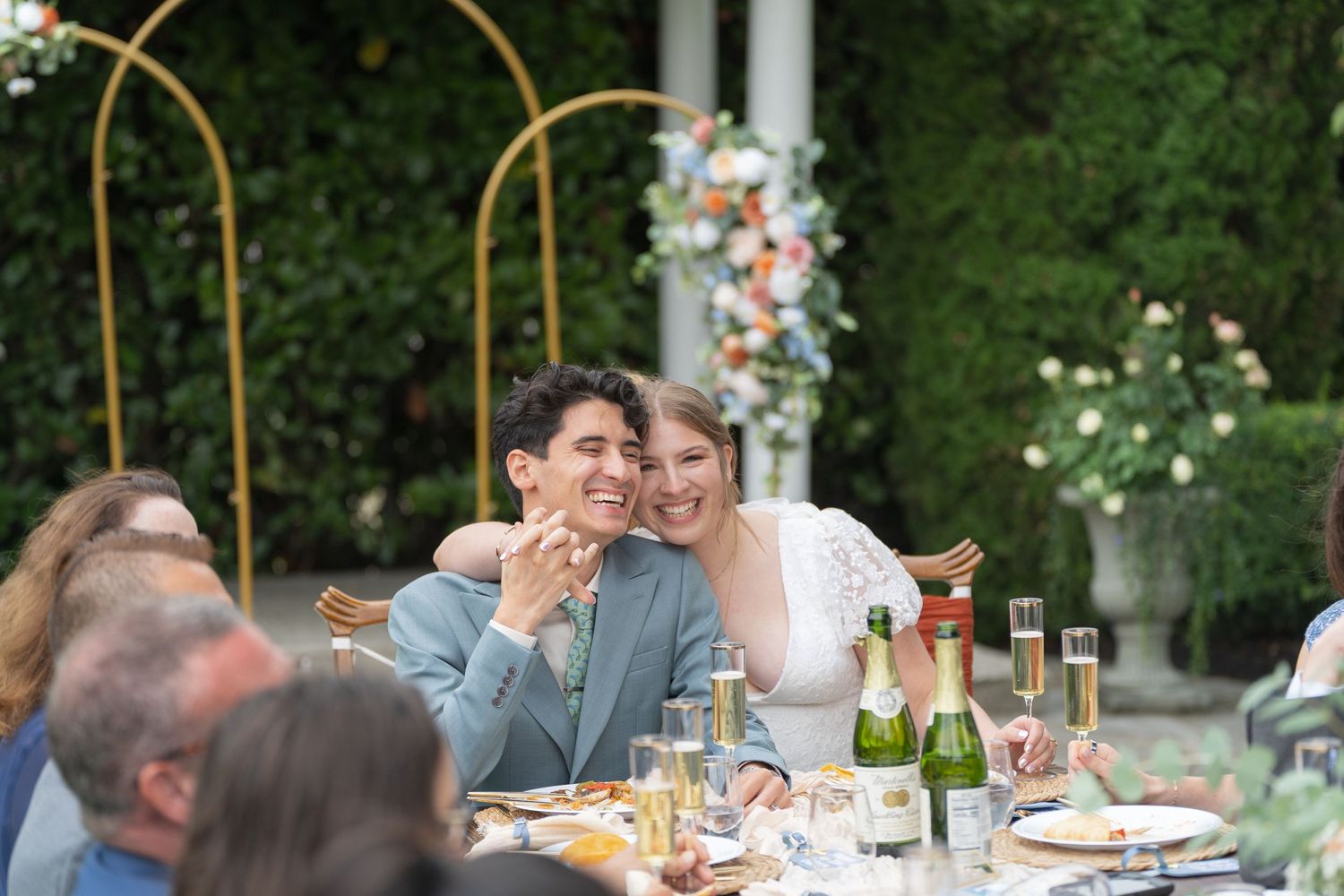 Wedding guests enjoy a casual outdoor dinner reception at long tables decorated with string lights and floral centerpieces.