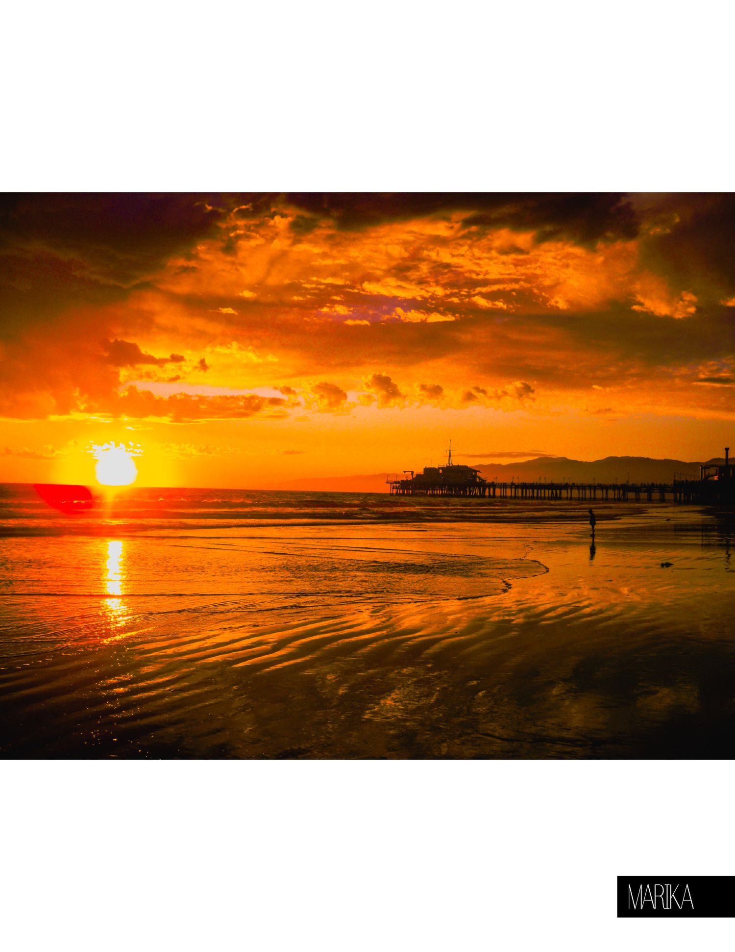 Dramatic orange and red sunset over ocean pier with silhouetted horizon and reflective water surface.