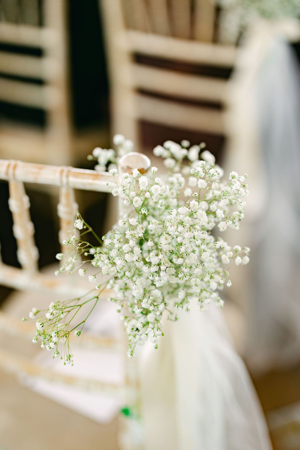 Delicate baby's breath flowers tied with white fabric to a wooden chair, creating an elegant wedding ceremony decoration.