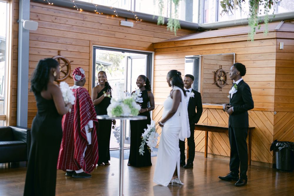 People in formal attire gather in a wooden-paneled room during what appears to be a wedding ceremony.