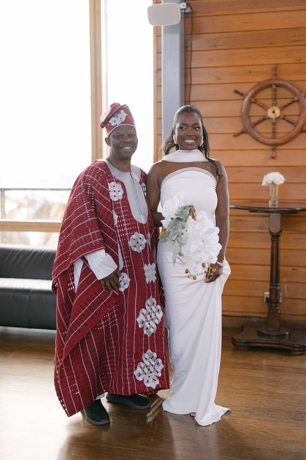 A wedding couple stands together on a wooden floor with decorative nautical elements visible in the background.