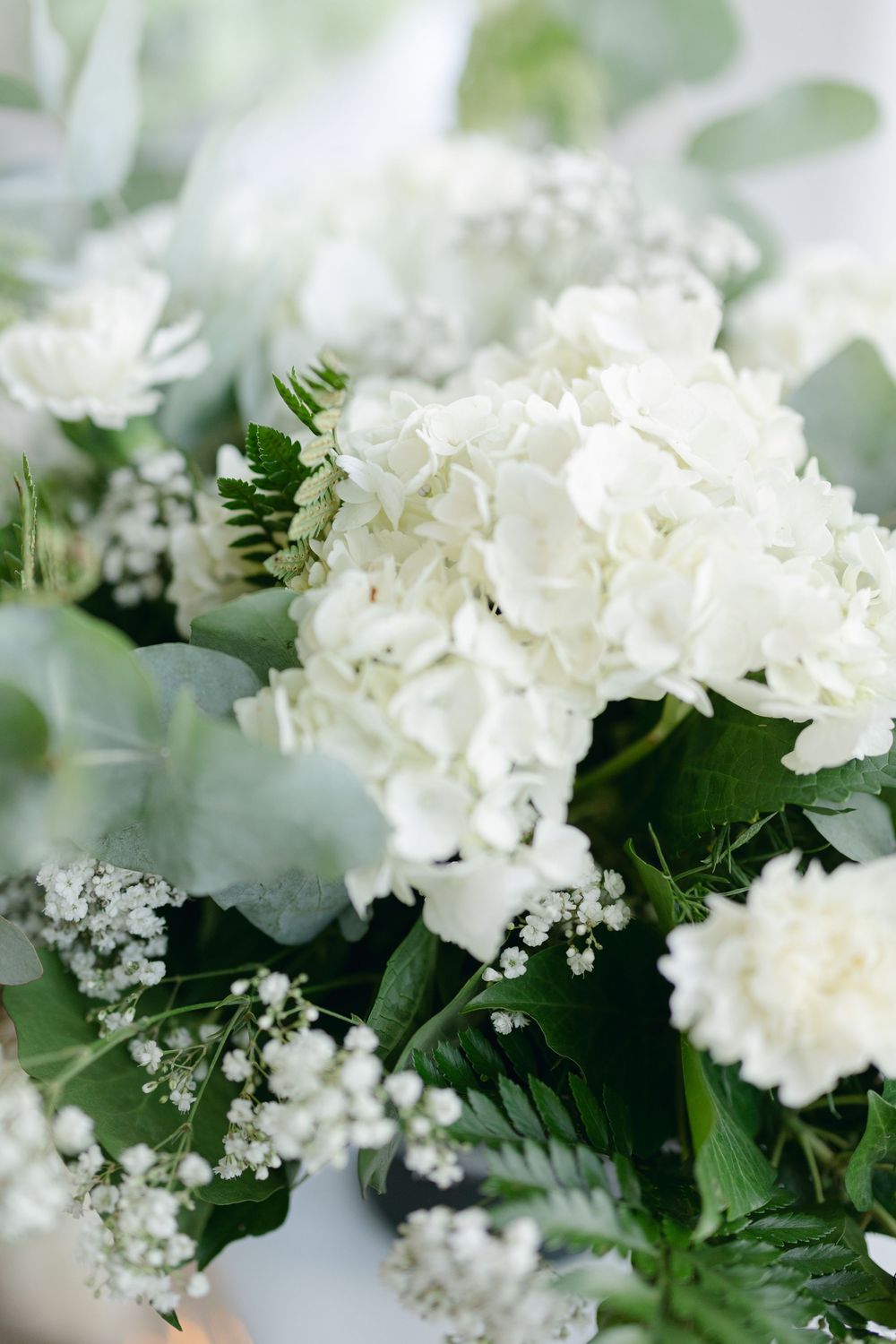 Close-up of white hydrangeas and baby's breath flowers with green foliage in an elegant floral arrangement.
