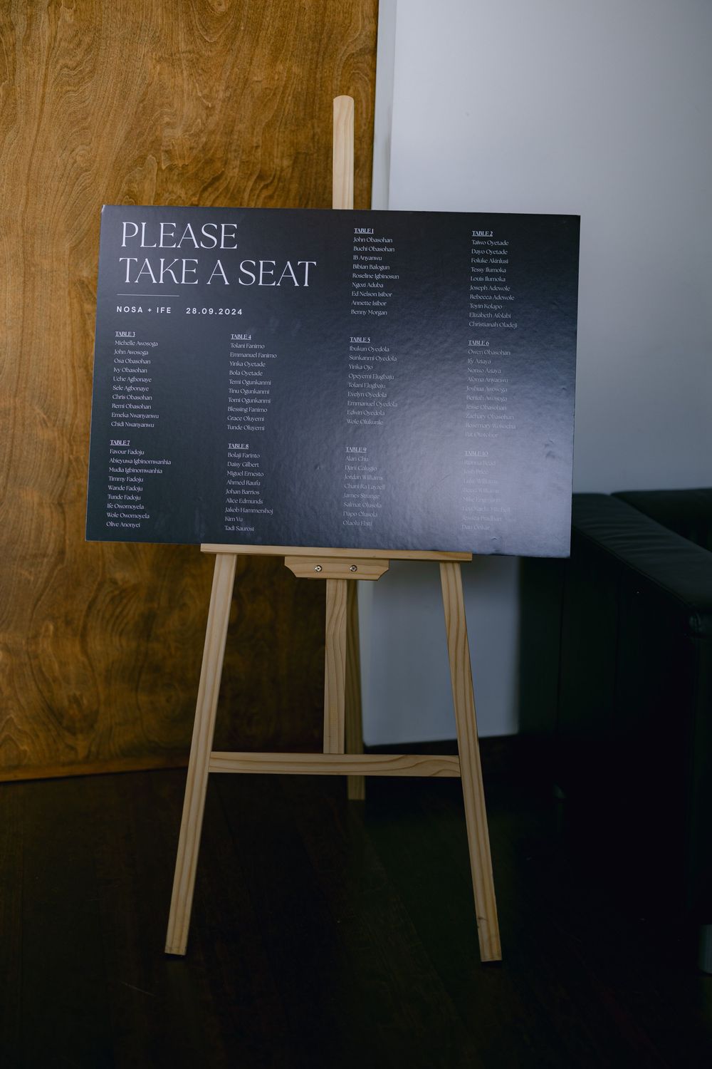 Wedding seating chart displayed on wooden easels with dark gray signage against a brown textured wall.