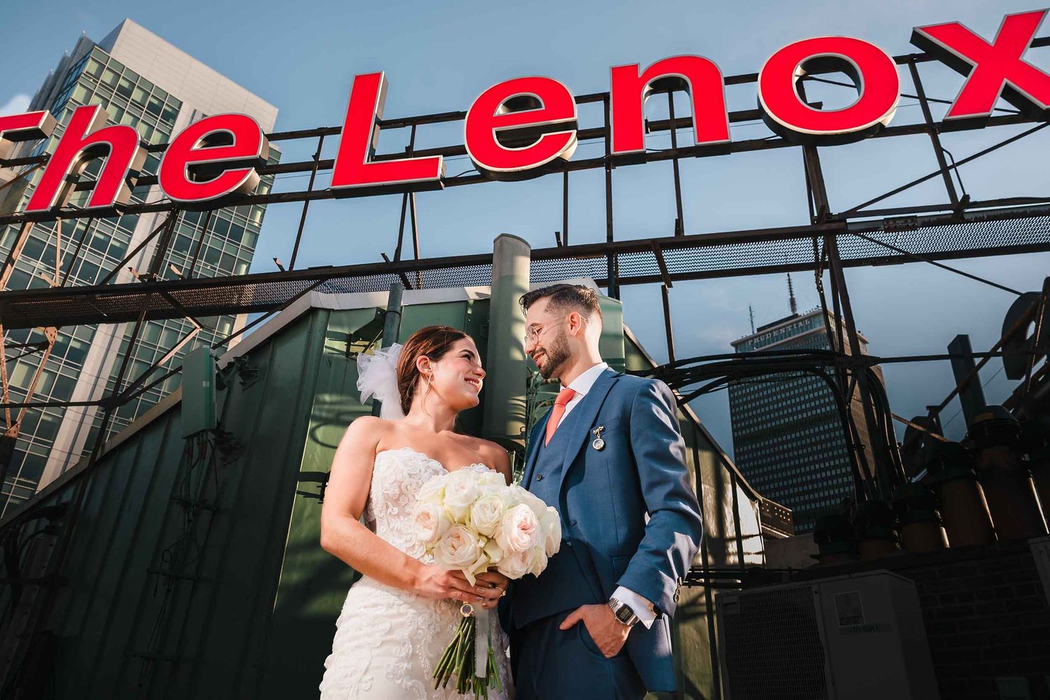 Bride and groom posing beneath the Lenox Hotel rooftop sign during wedding portraits in Boston