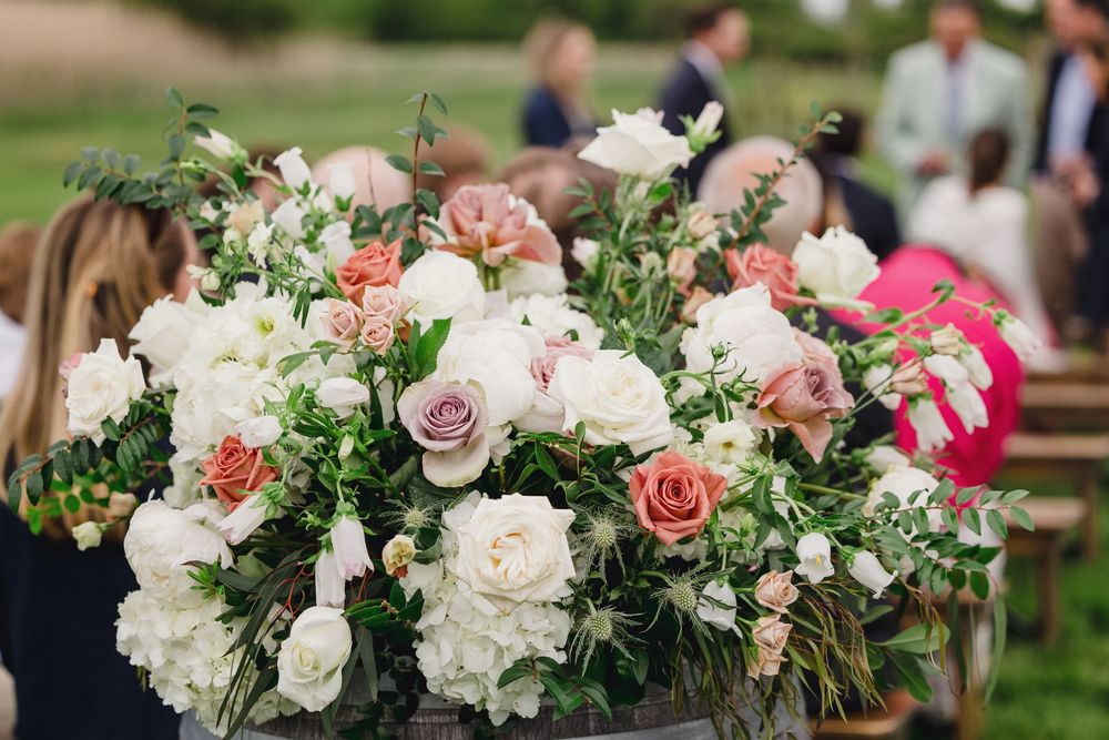 Elegant wedding floral arrangements featuring pink and white roses with greenery displayed at an outdoor reception.
