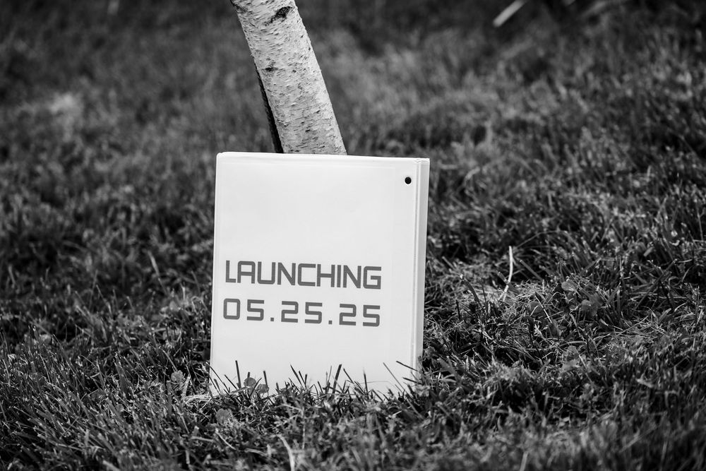 A row of small white signs with text and numbers are placed in grass or soil.