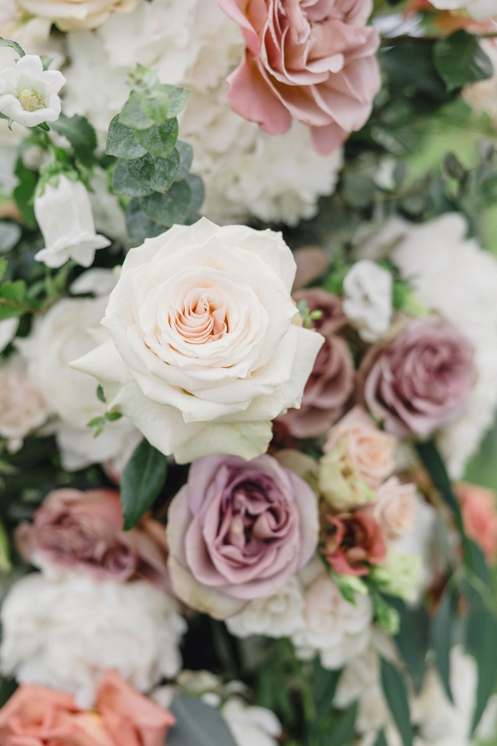 Close-up of romantic wedding bouquet featuring blush pink and white roses with delicate greenery.