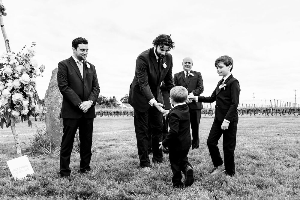 Black and white photo of a wedding ceremony moment with guests gathered on grassy field.