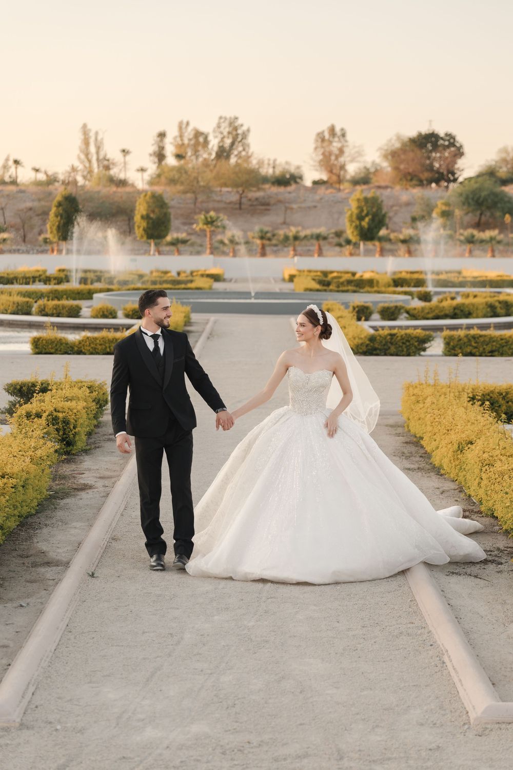 A bride and groom share a romantic moment on a path surrounded by manicured gardens.