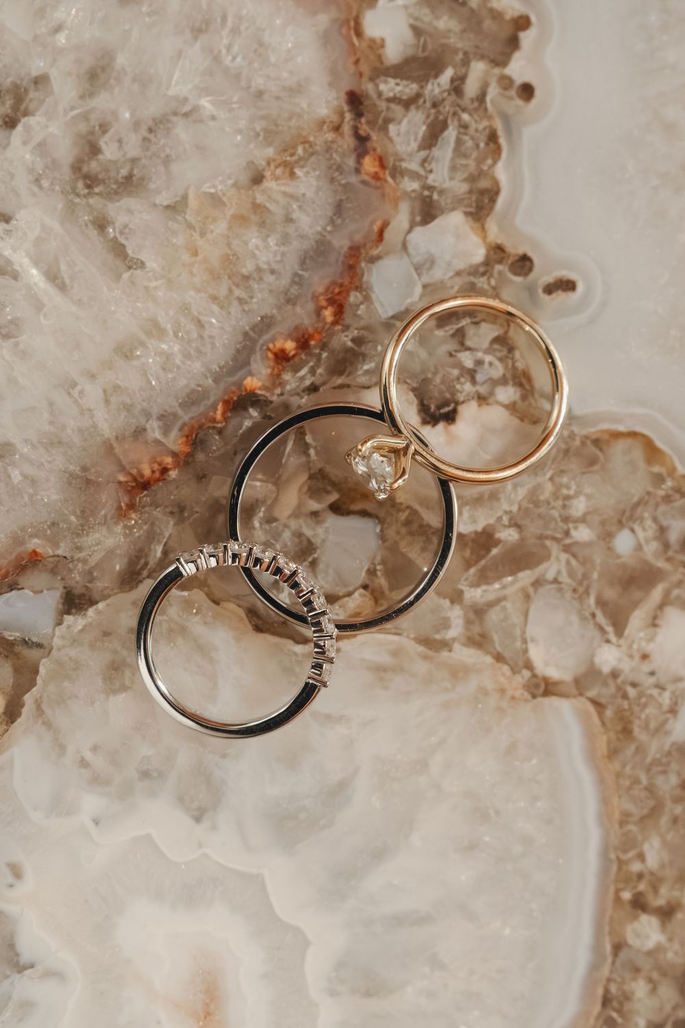 Wedding rings photographed on textured marble surface with warm tones and artistic composition.