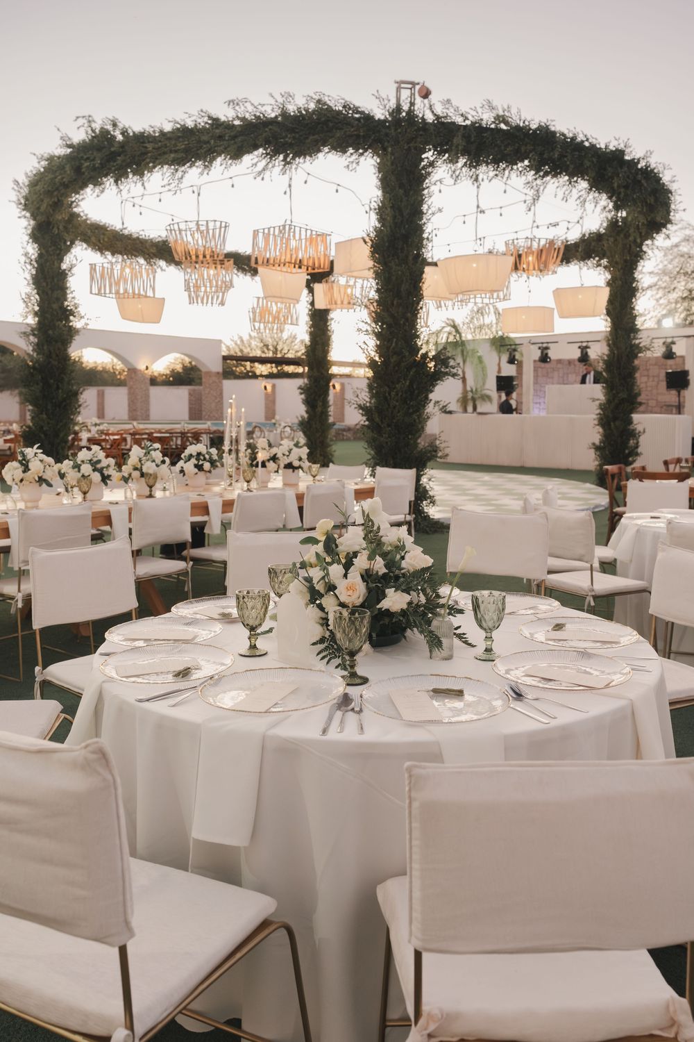 An elegant outdoor wedding reception setup with greenery arches and white table settings.